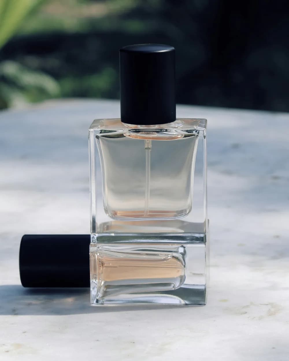 A clear glass perfume bottle with a black cap on stone